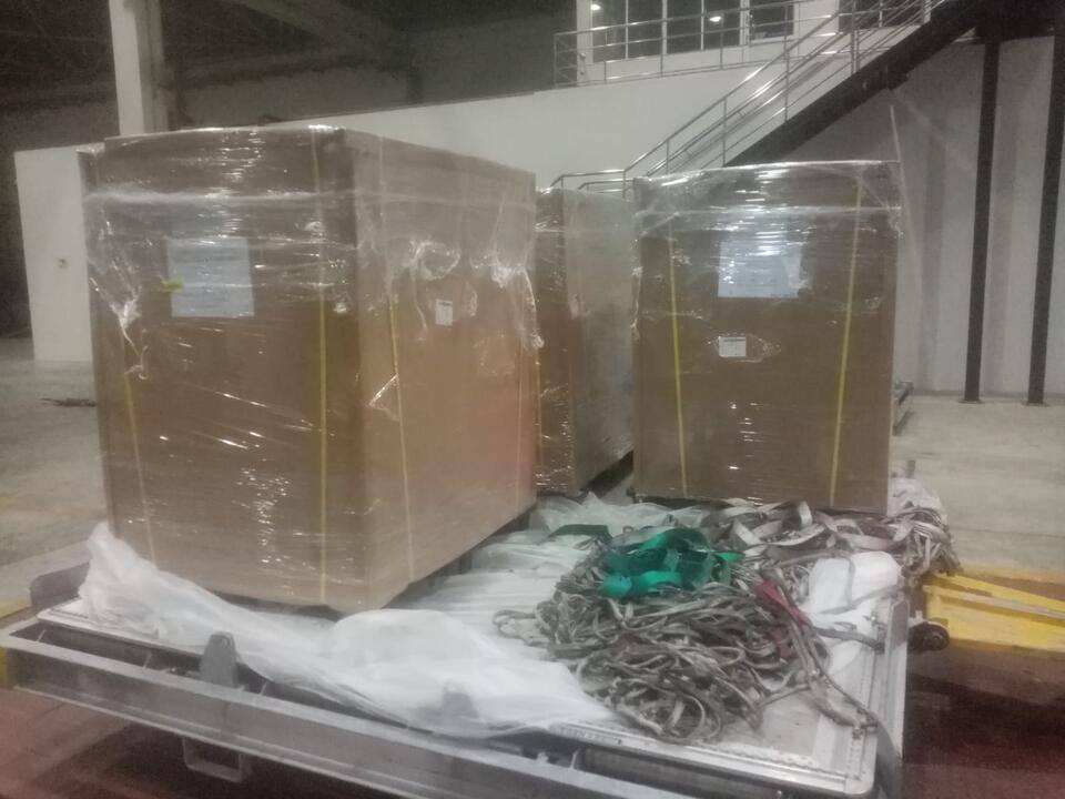 Large wrapped cartons loaded on a metal cargo pallet with netting beside them