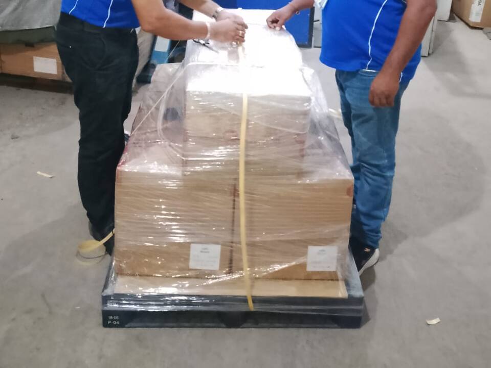 Two people fastening a strap around a shrink-wrapped pallet of cartons